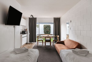 A compact living space with a kitchenette, a flat-screen TV, a dining area, and a sofa.