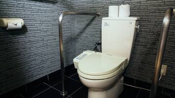 A modern bathroom with a toilet, a handrail, and a toilet paper dispenser.