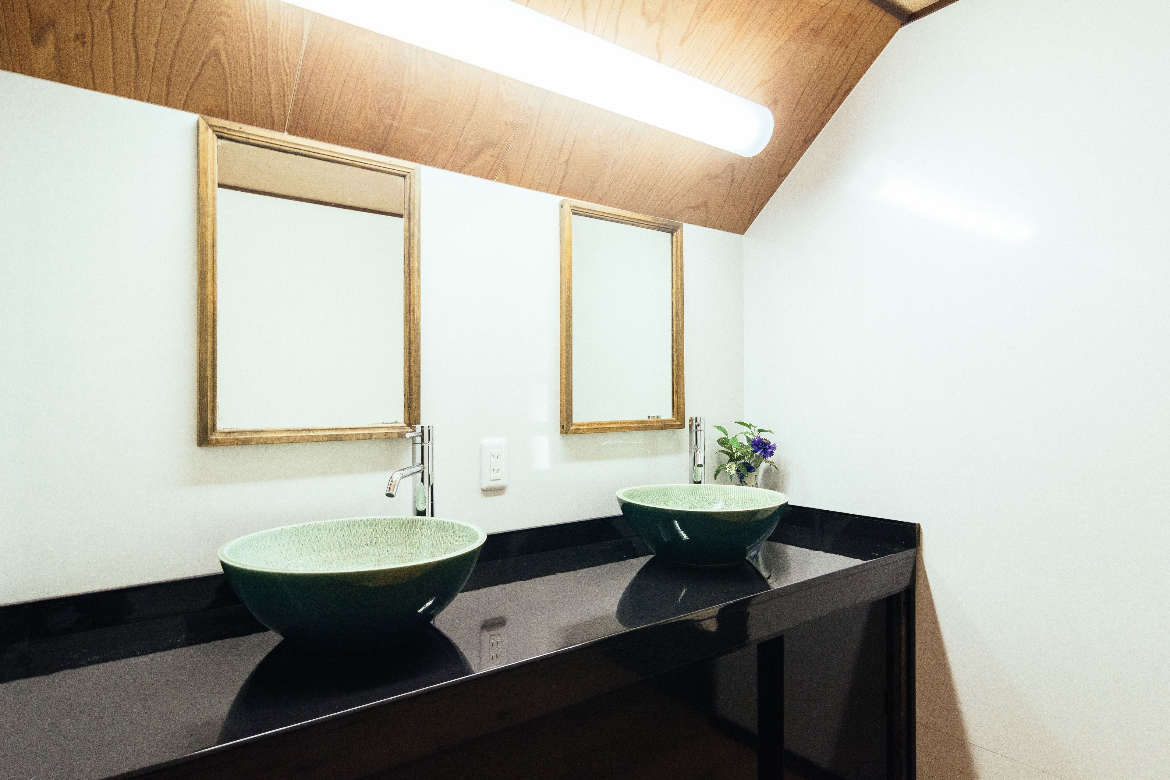 A bathroom with two green ceramic sinks, a black countertop, and wooden ceiling.