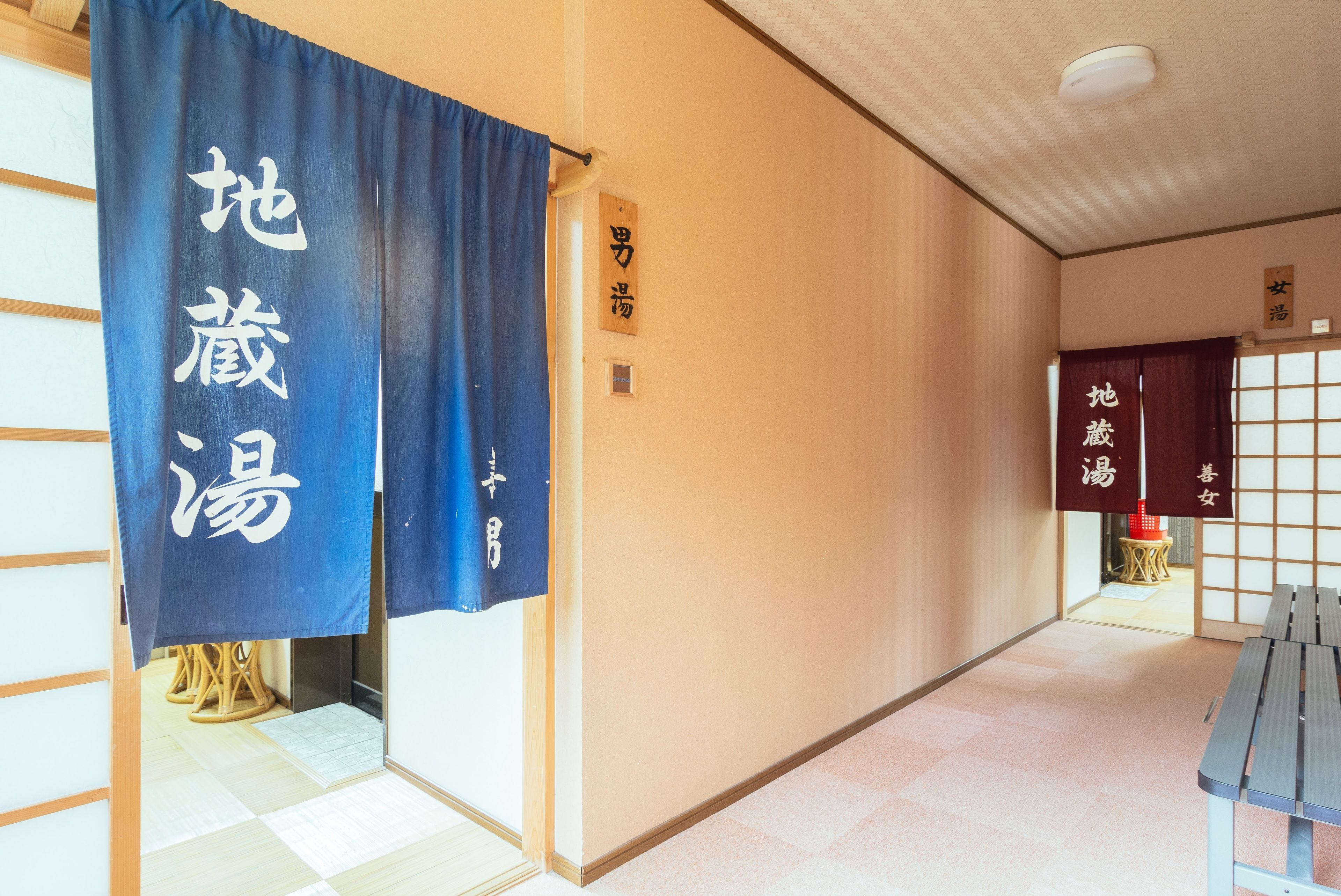 A hallway with tatami mat flooring, blue and red curtains with Japanese characters, and a wooden bench.