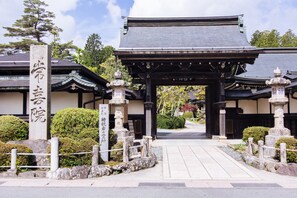 A traditional Japanese building with a tiled roof, stone lanterns, and a stone pillar with Japanese characters.