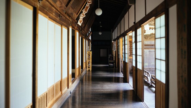 A traditional Japanese corridor with wooden beams, tatami flooring, sliding doors, and a hanging light fixture. - Jokiin (Koya)