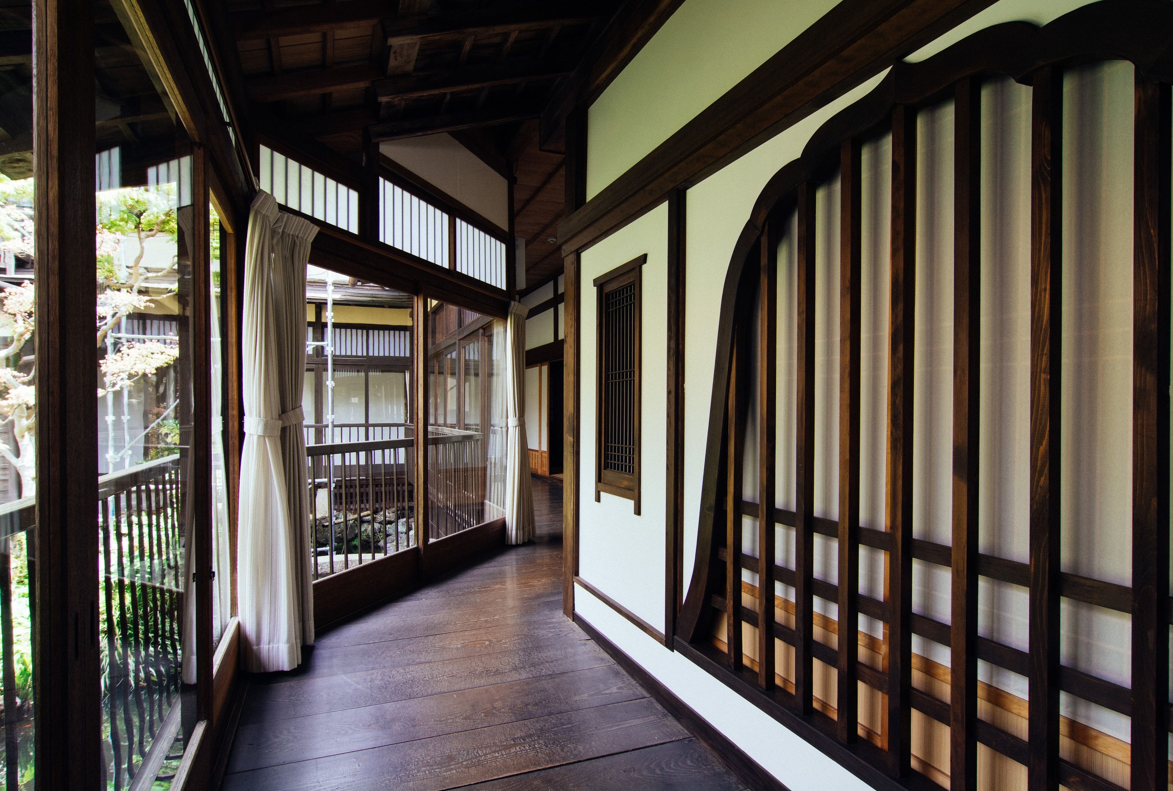 En traditionell japansk korridor med trägolv, skjutdörrar och utsikt över en trädgård.