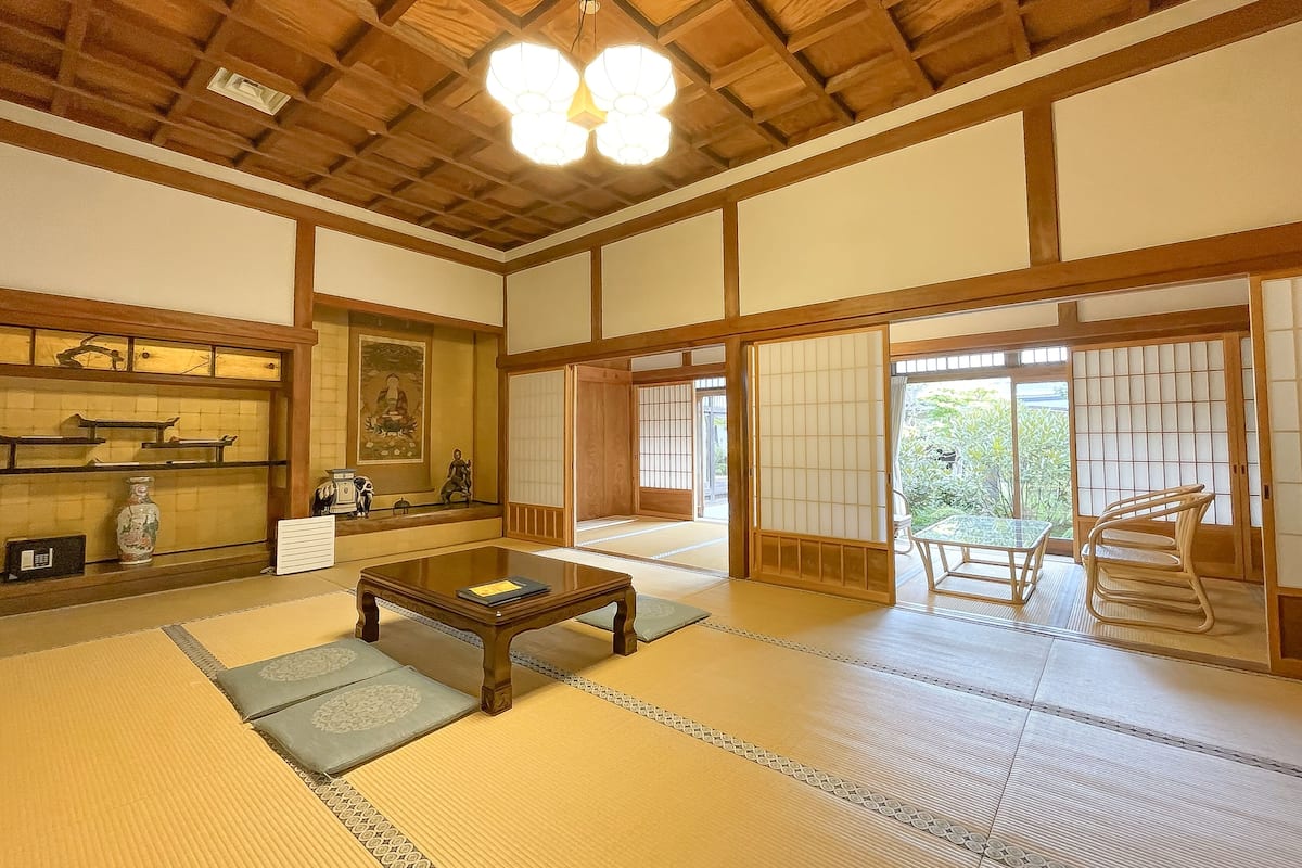 A traditional Japanese room with tatami flooring, a low wooden table, and sliding doors leading to a garden.