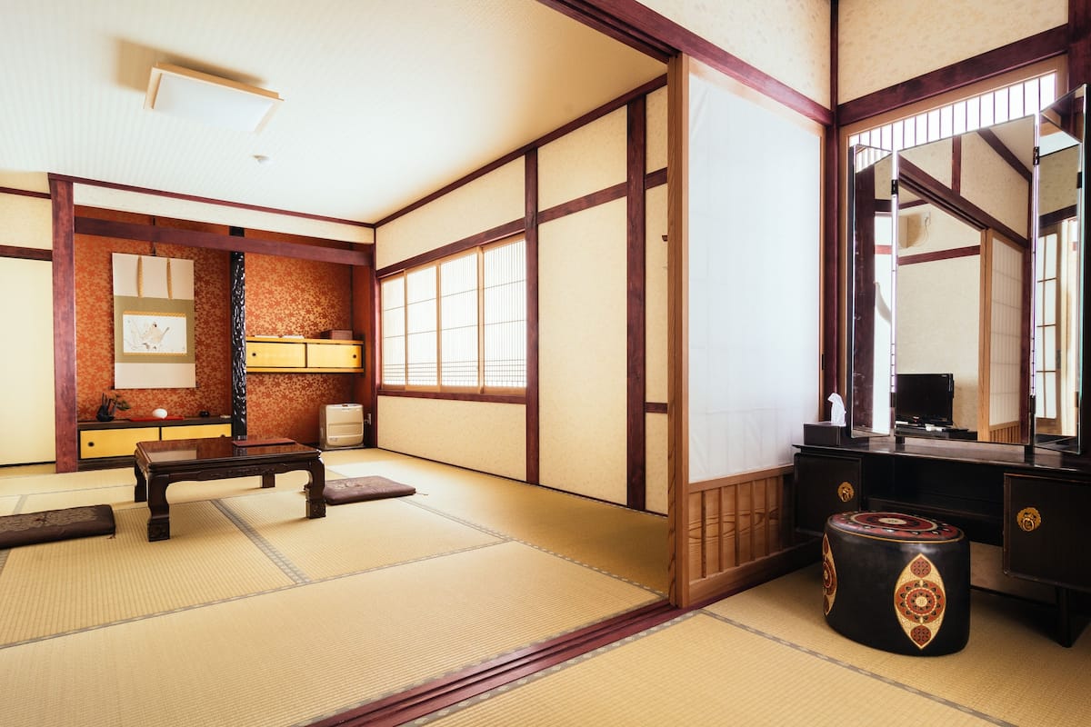 A traditional Japanese room with tatami flooring, a low wooden table, a cushioned bench, a dark wooden cabinet, and a large mirror.