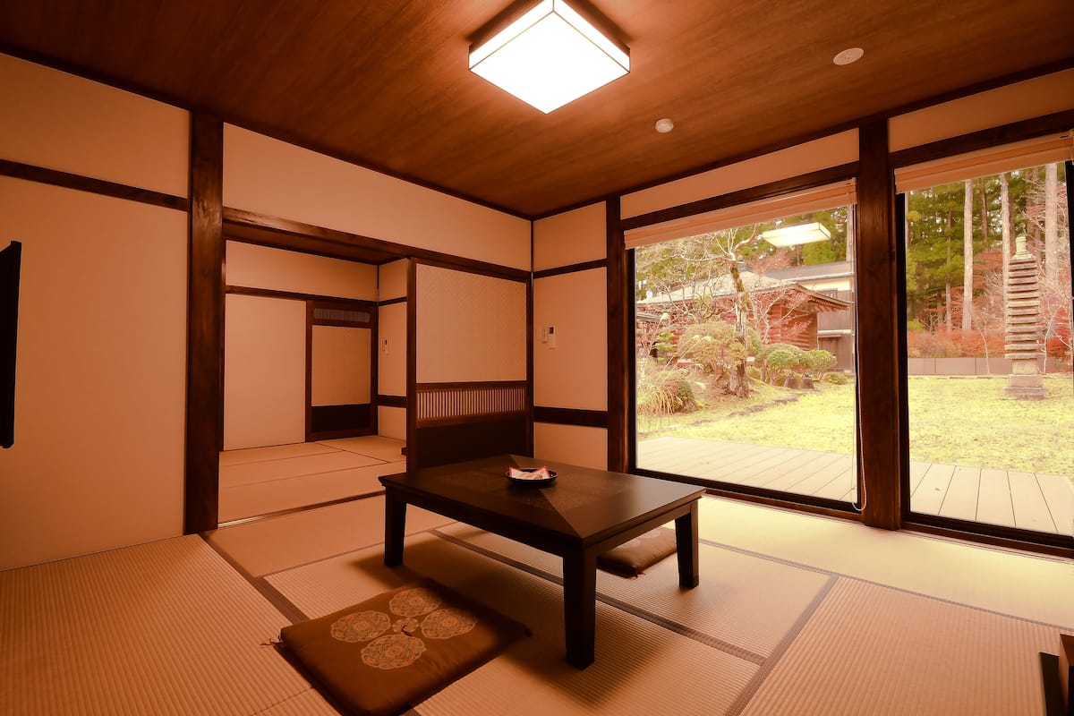 A traditional Japanese room with tatami flooring, a low wooden table, and a sliding door leading to an outdoor garden.