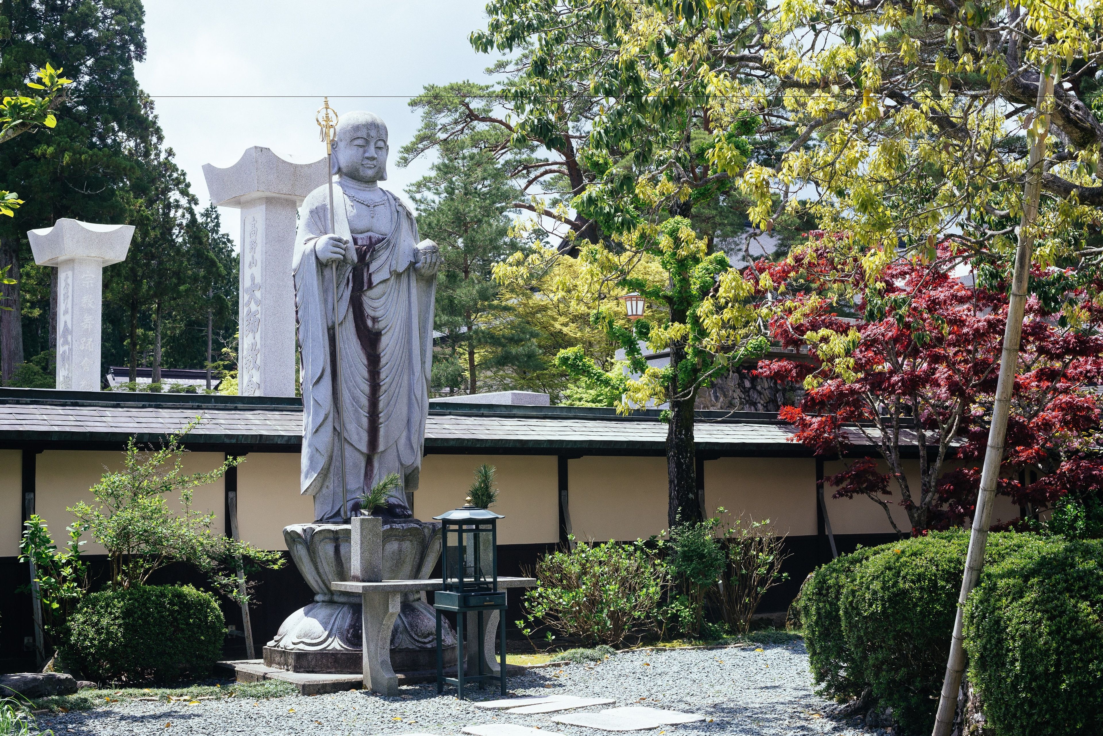 Eine Statue in einem Garten, im Hintergrund ein traditionelles Gebäude.
