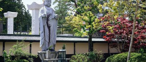 Eine Statue in einem Garten, im Hintergrund ein traditionelles Gebäude.