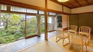 A traditional Japanese room with tatami flooring, wooden furniture, and large windows overlooking a garden. - Jokiin (Koya)
