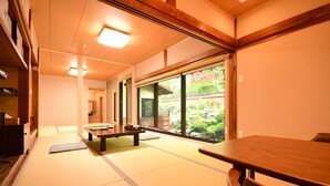 A traditional Japanese room with tatami flooring, wooden furniture, and large windows offering a view of greenery. - Jokiin (Koya)