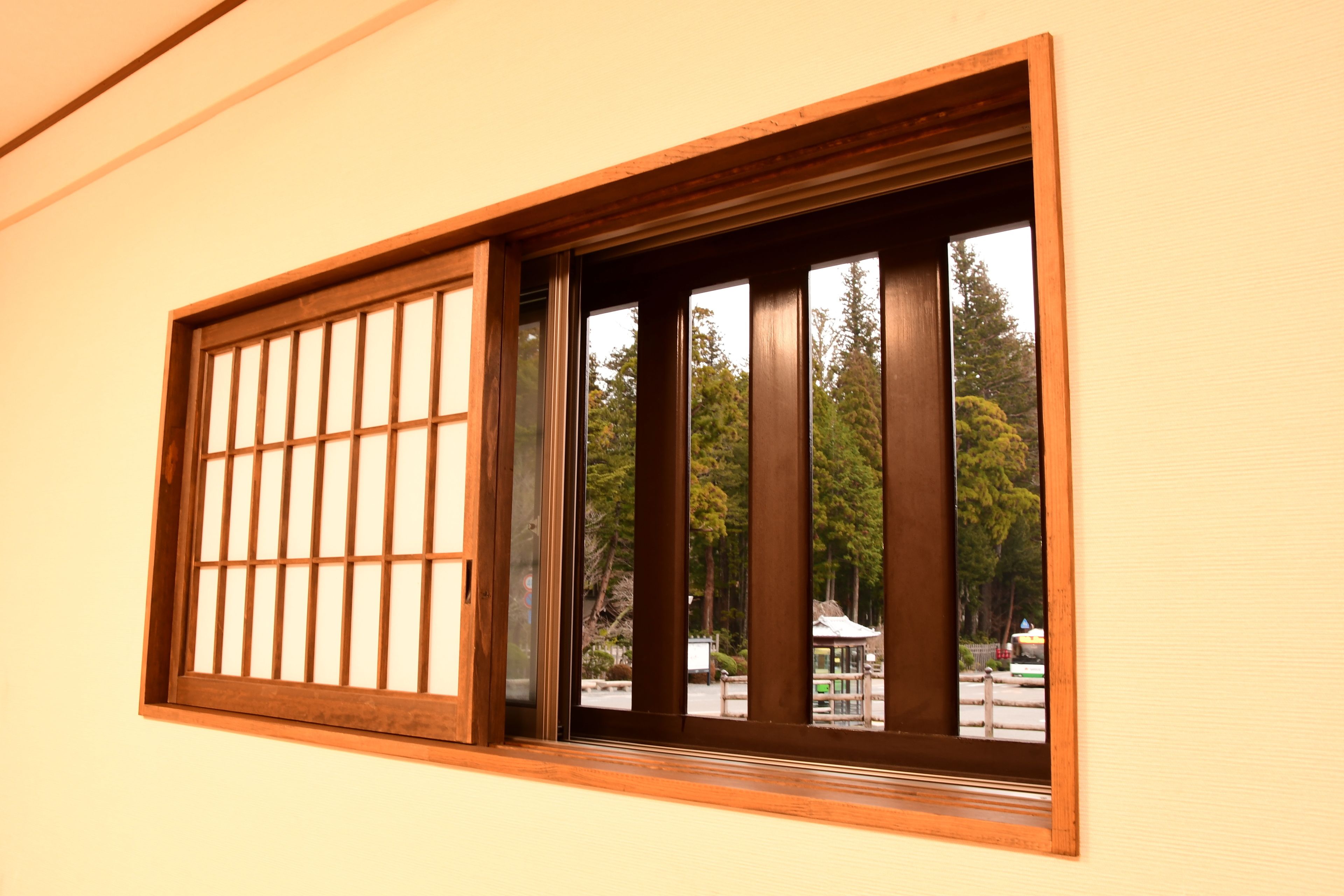 A window with a traditional wooden frame and grid pattern, offering a view of a park with trees and a gazebo.