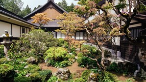 A traditional Japanese garden with a building featuring a tiled roof and wooden walls. - Jokiin (Koya)