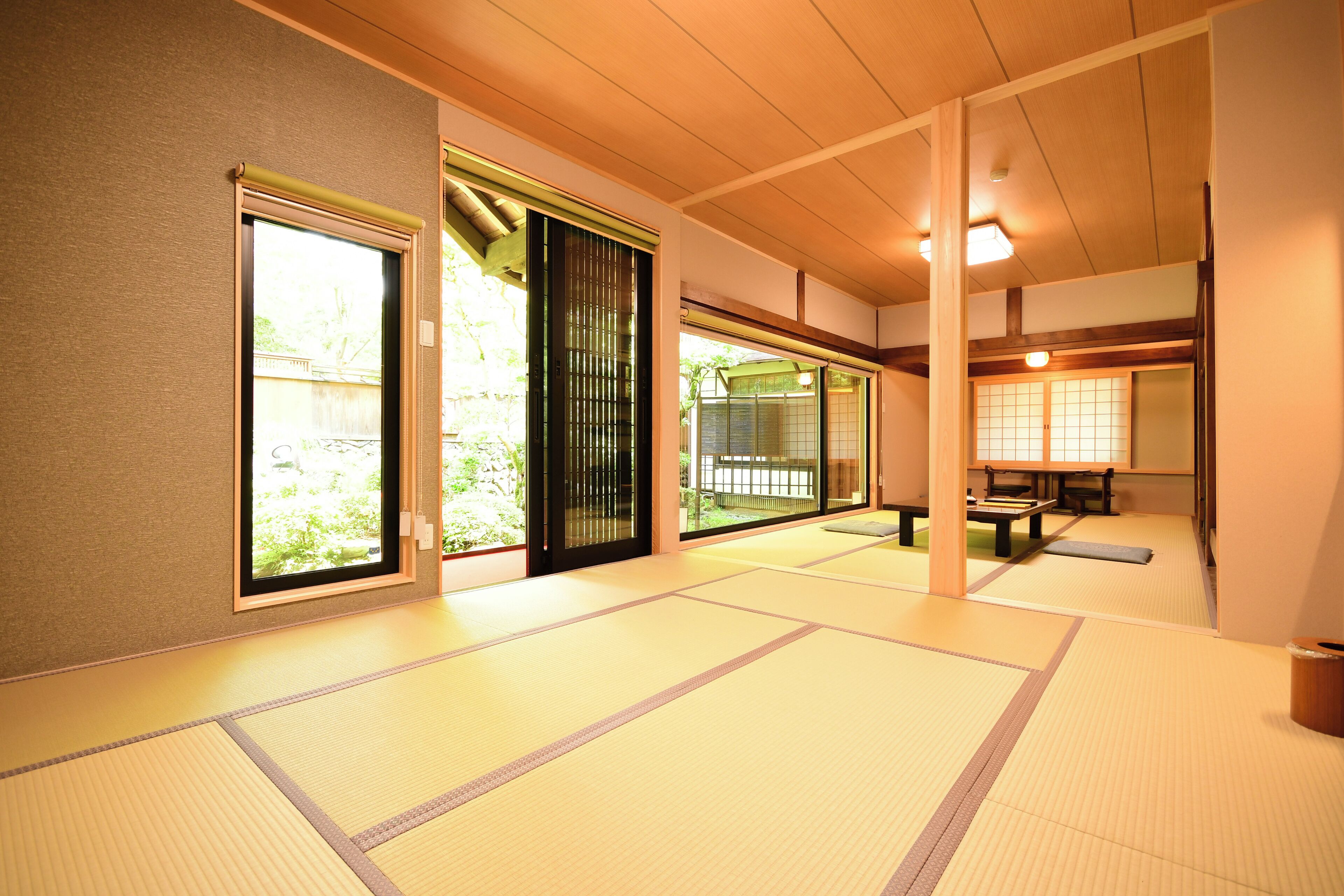 Una habitación japonesa tradicional con suelo de tatami, puertas correderas y vistas a un jardín.