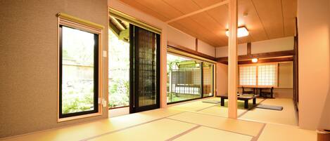 Una habitación japonesa tradicional con suelo de tatami, puertas correderas y vistas a un jardín.