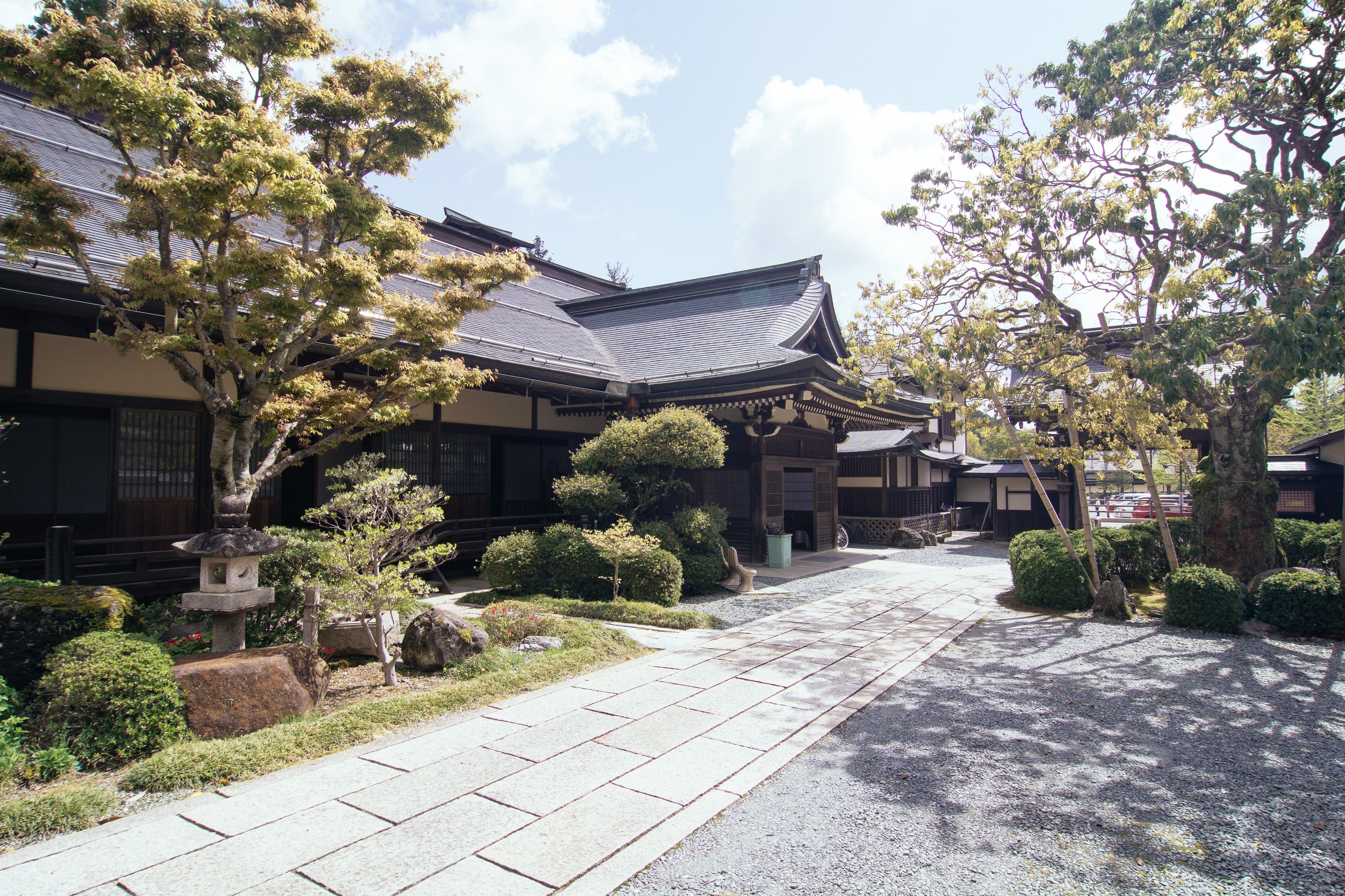 A traditional Japanese building with a tiled roof, surrounded by well-maintained gardens and a gravel pathway.