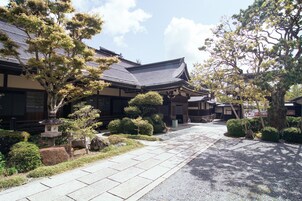 Un edificio japonés tradicional con techo de tejas, rodeado de jardines cuidados y un sendero de grava.
