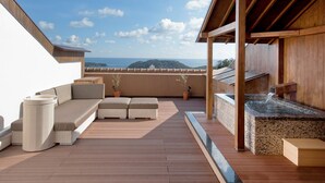 Een houten terras met een zitgedeelte, een jacuzzi en uitzicht op de oceaan.