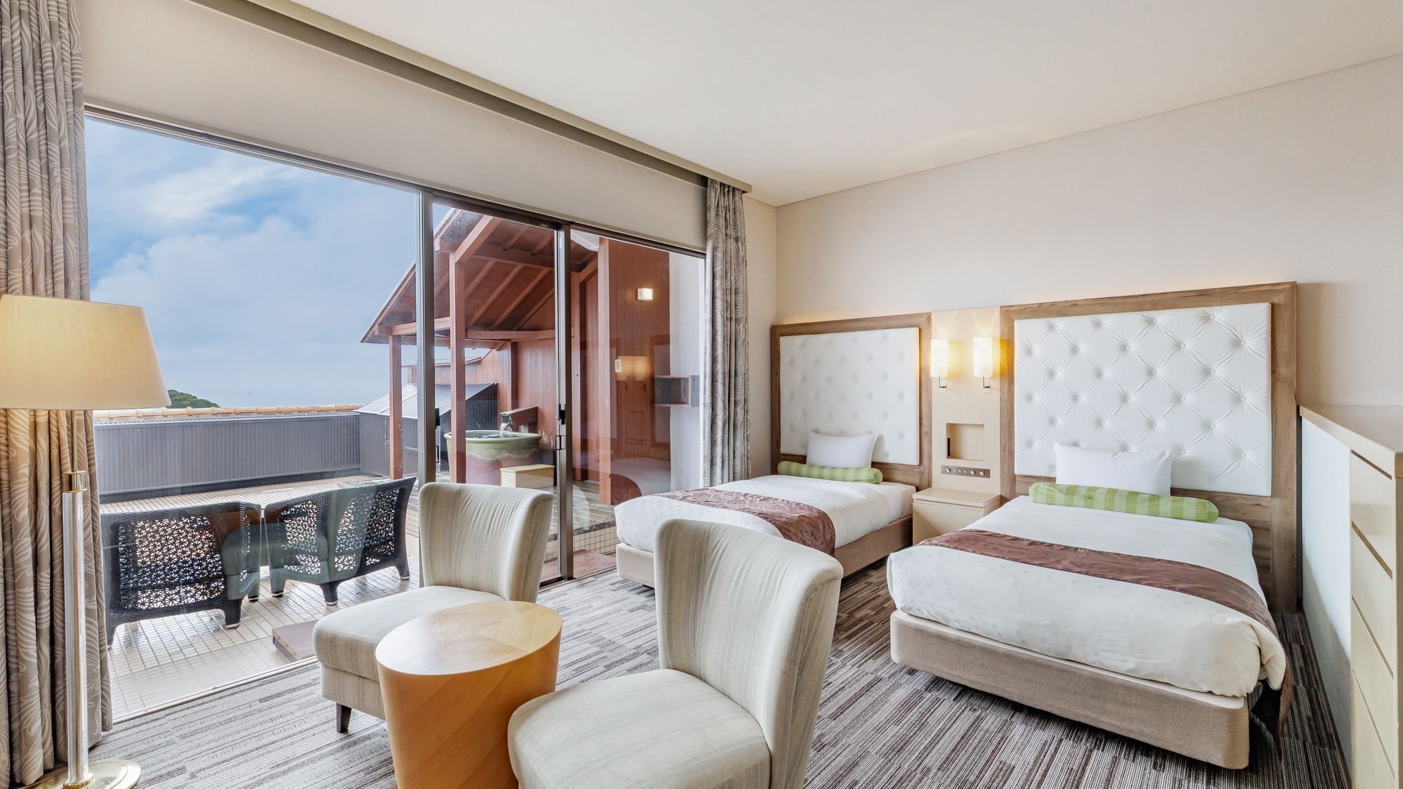 Habitación de hotel con dos camas, un balcón, una silla y una pequeña mesa.