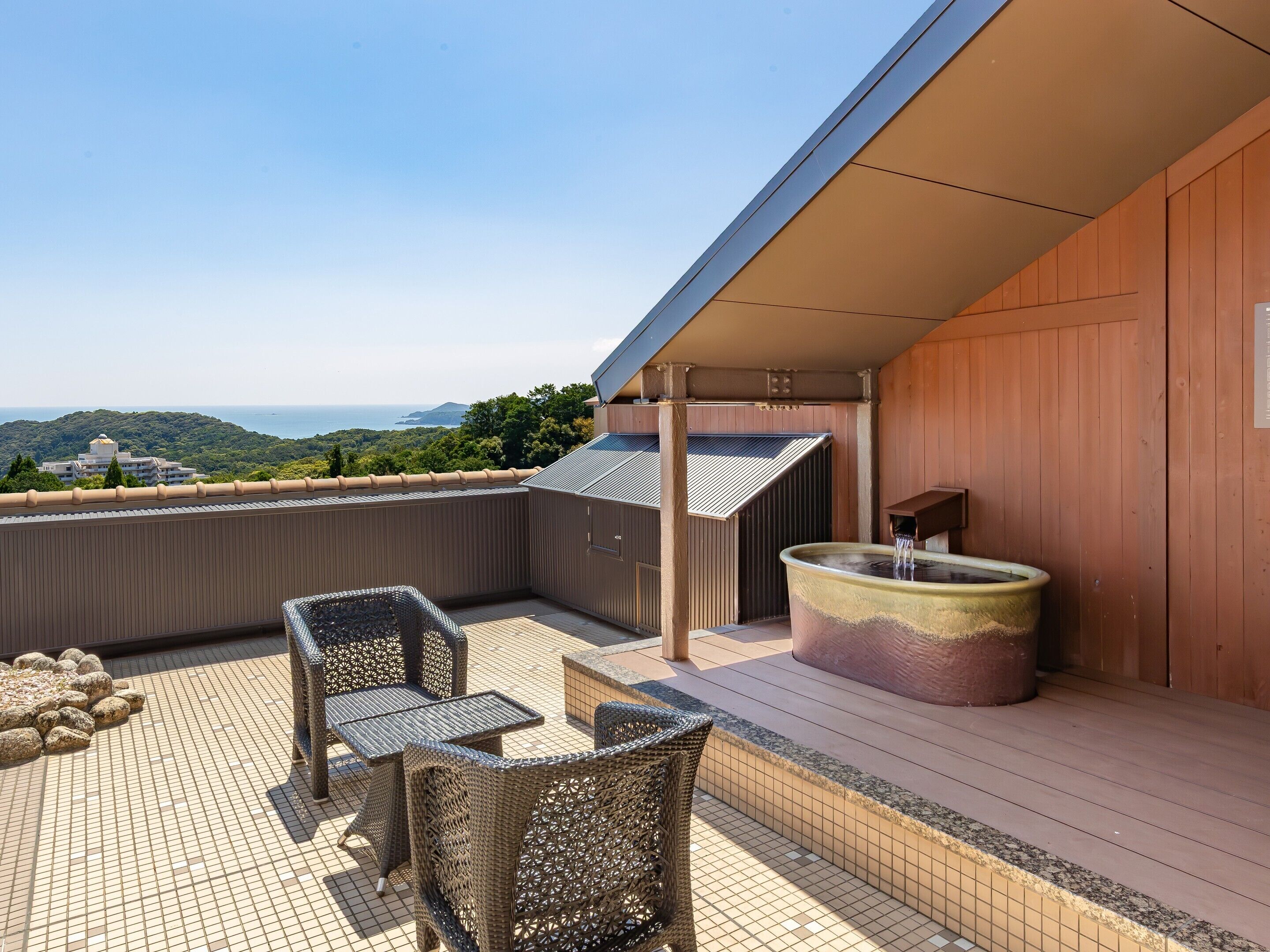 Um terraço no telhado com móveis de vime, um grande vaso de plantas e vista para o mar.