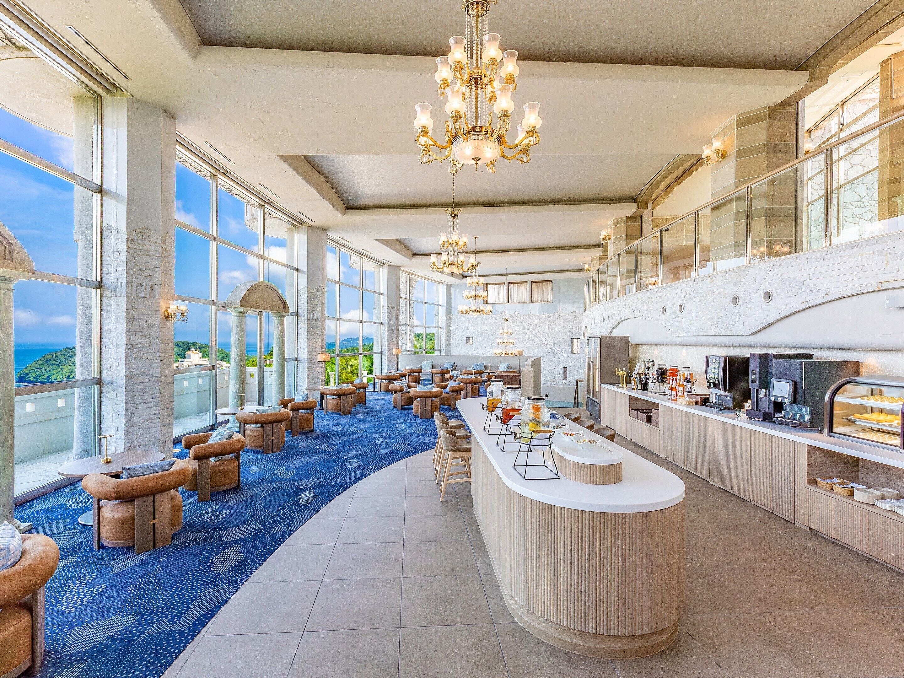 A spacious lounge area with a long counter, comfortable seating, and large windows offering a view of the sea.