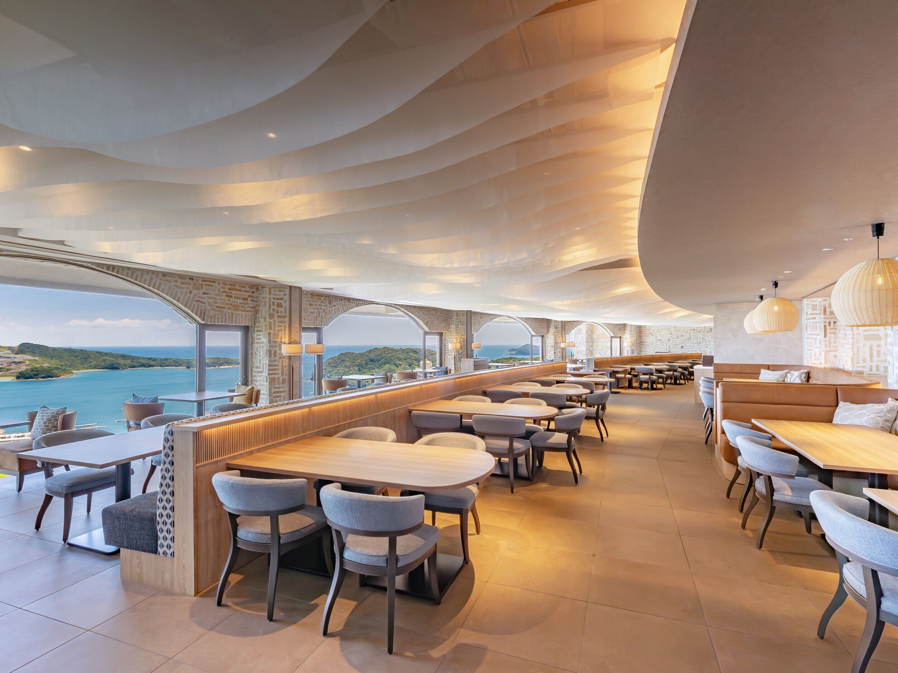 A modern restaurant with a view of the sea, featuring a bar area, seating arrangements, and contemporary lighting fixtures.