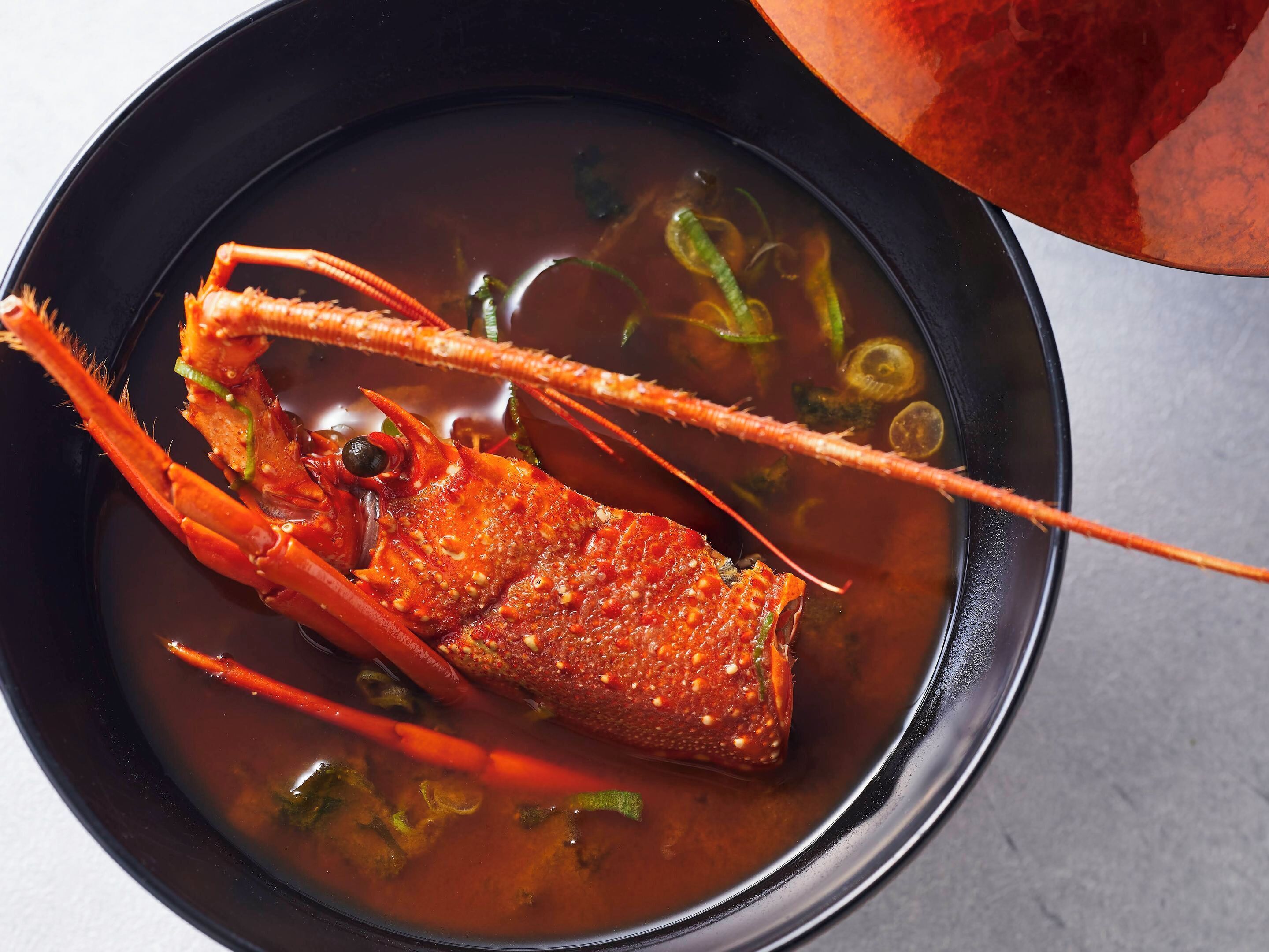 Un tazón de sopa con una pata de cangrejo, cebolletas y un chile rojo.