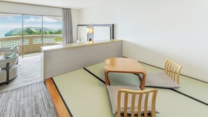 Hotelkamer met tatami vloerbedekking, een houten tafel, stoelen, een bank, een balkon met uitzicht en een plafondlamp.