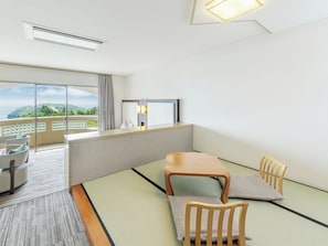 Habitación de hotel con suelo de tatami, una mesa de madera, sillas, un sofá, un balcón con vistas y una lámpara de techo.