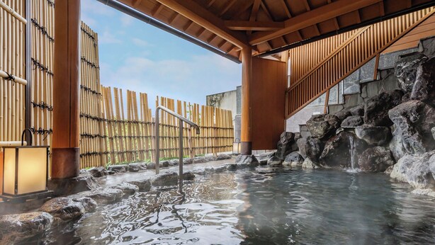 Een warmwaterbronnengebied met een houten constructie, bamboomschutting en een waterval van steen.