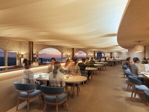 Un restaurante con mesas redondas y sillas azules, amplios ventanales con vistas y una pared de piedra.
