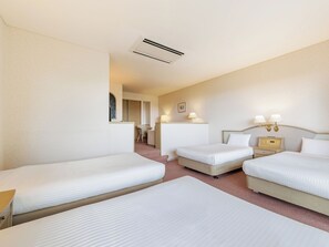 A hotel room with three beds, a desk, a chair, and a small table with lamps.
