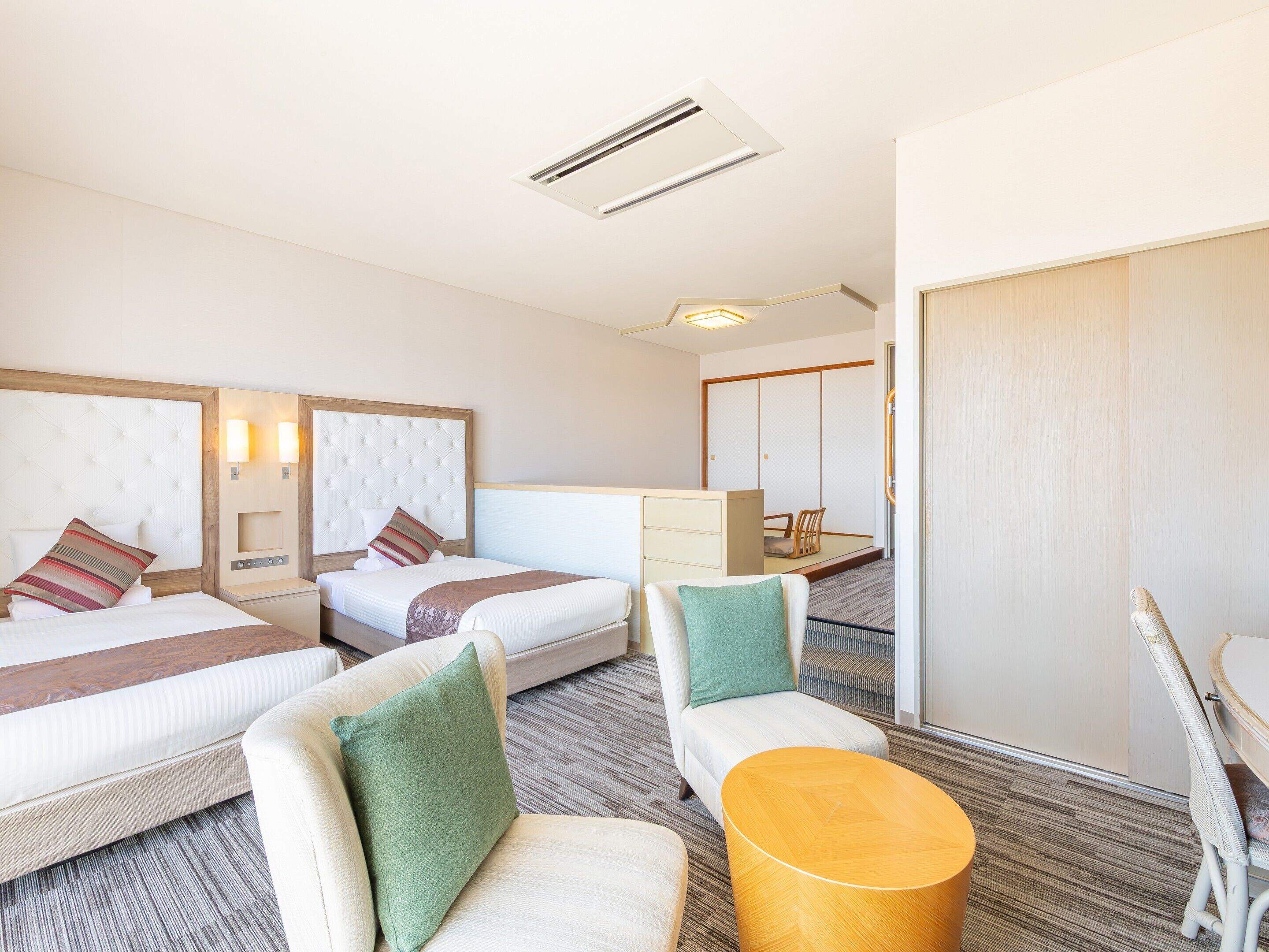 A hotel room with two beds, a seating area with chairs, a small table, and a sliding door leading to a closet.