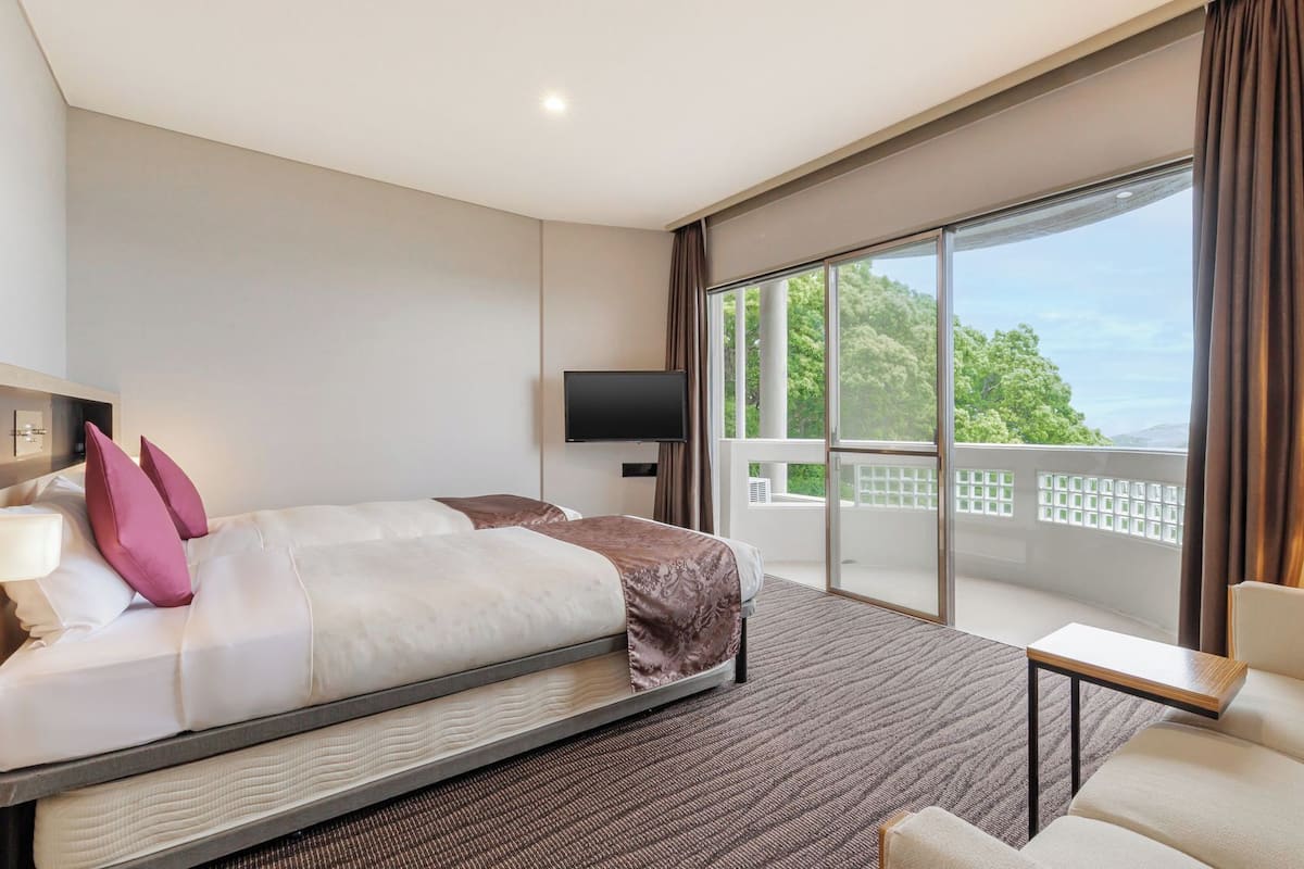 Habitación de hotel con cama, televisor, balcón y vistas, además de una silla.
