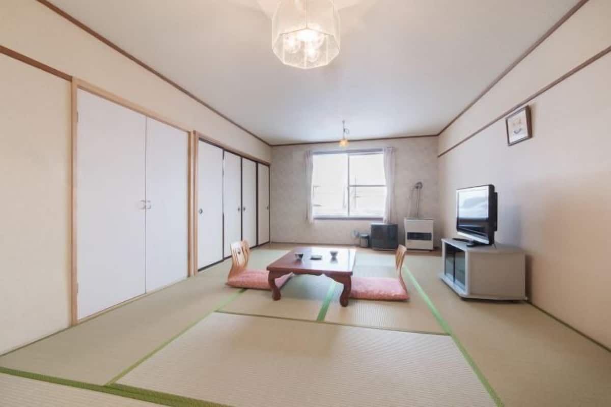 A traditional Japanese room with tatami flooring, a low table, a television, and sliding doors.