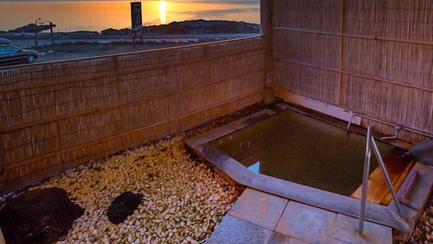 En träkonstruktion med utsikt över solnedgången över vattnet, ett bubbelbad och ett område med småsten.