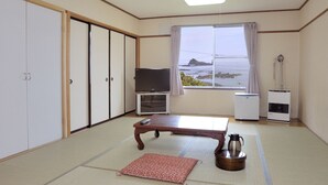 Ett rum med tatamimattor på golvet, ett lågt bord, en tv, en värmare och utsikt över havet.