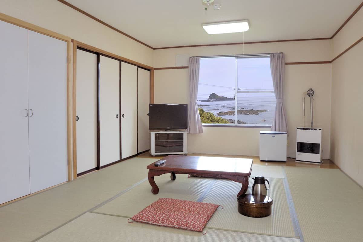 A room with tatami flooring, a low table, a television, a heater, and a view of the sea.