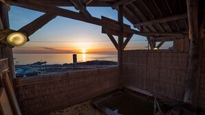En träkonstruktion med utsikt över solnedgången över ett vattendrag, ett bubbelbad och ett trästaket.