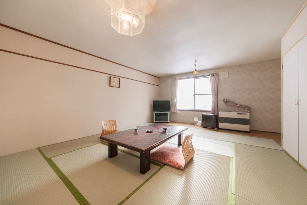 A room with tatami flooring, a low table, a television, and a heater.