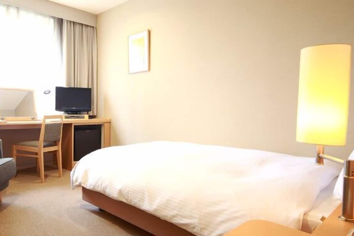 Ein Hotelzimmer mit Bett, Schreibtisch, Stuhl, Fernseher und Lampe.