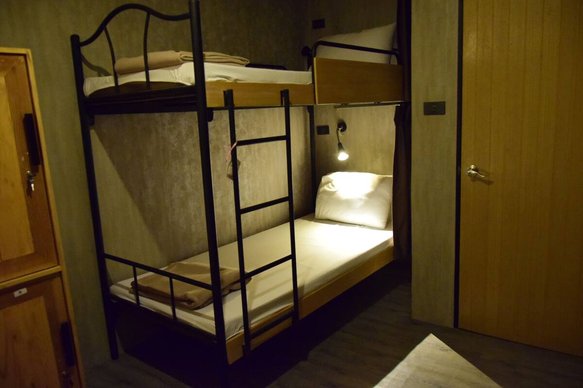 A bunk bed room with a wooden door, a small desk, and a bedside lamp.