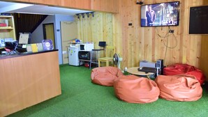 A room with a wooden interior, a television mounted on the wall, a desk with a computer, and bean bags.