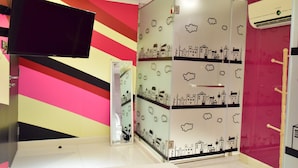 A hotel room with a TV mounted on the wall, a mirror, and a wardrobe with cloud and cityscape decals.