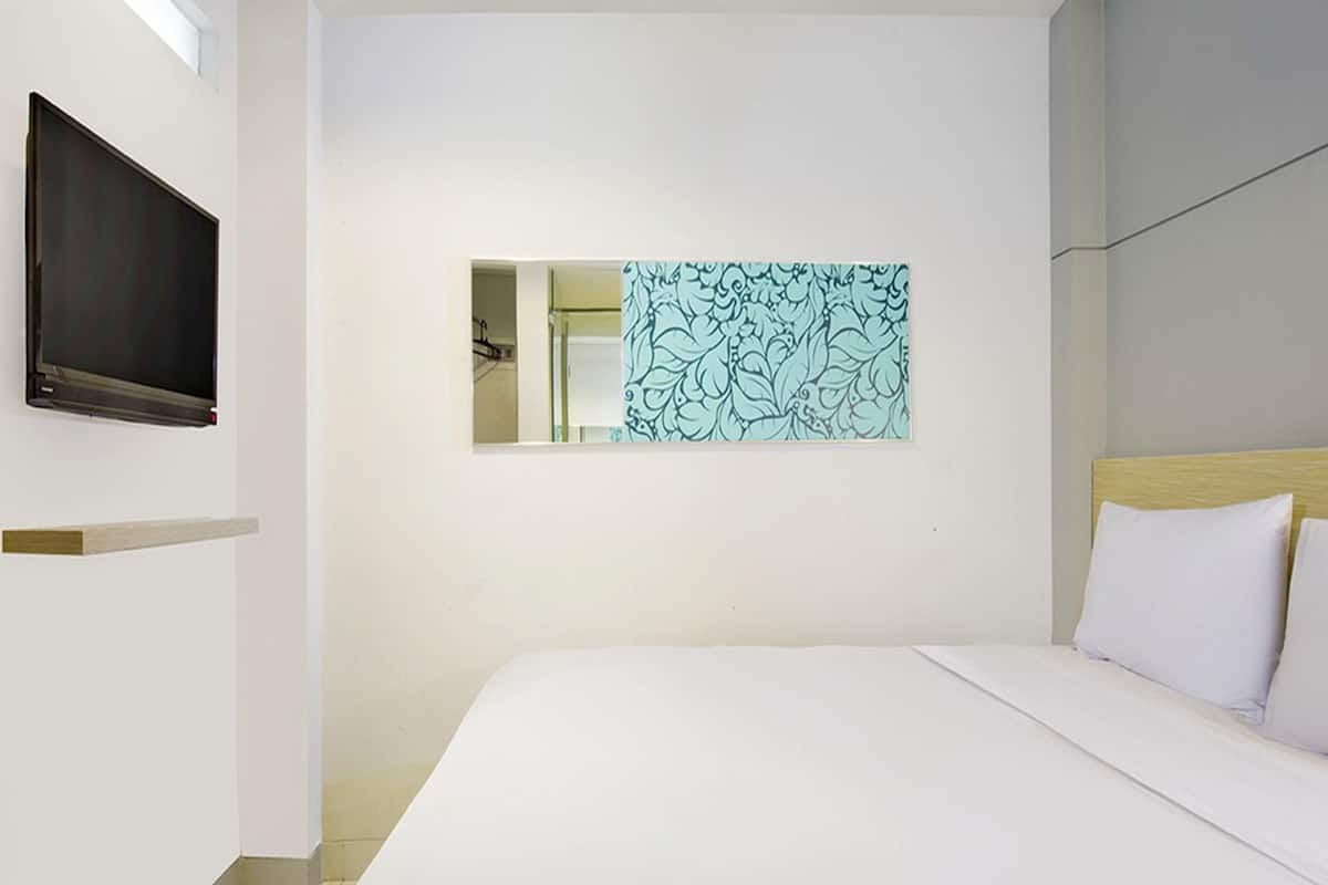 A hotel room with a bed, a TV mounted on the wall, and a decorative mirror.