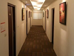 Pasillo de hotel con alfombra estampada, obras de arte enmarcadas en las paredes y puertas a ambos lados.