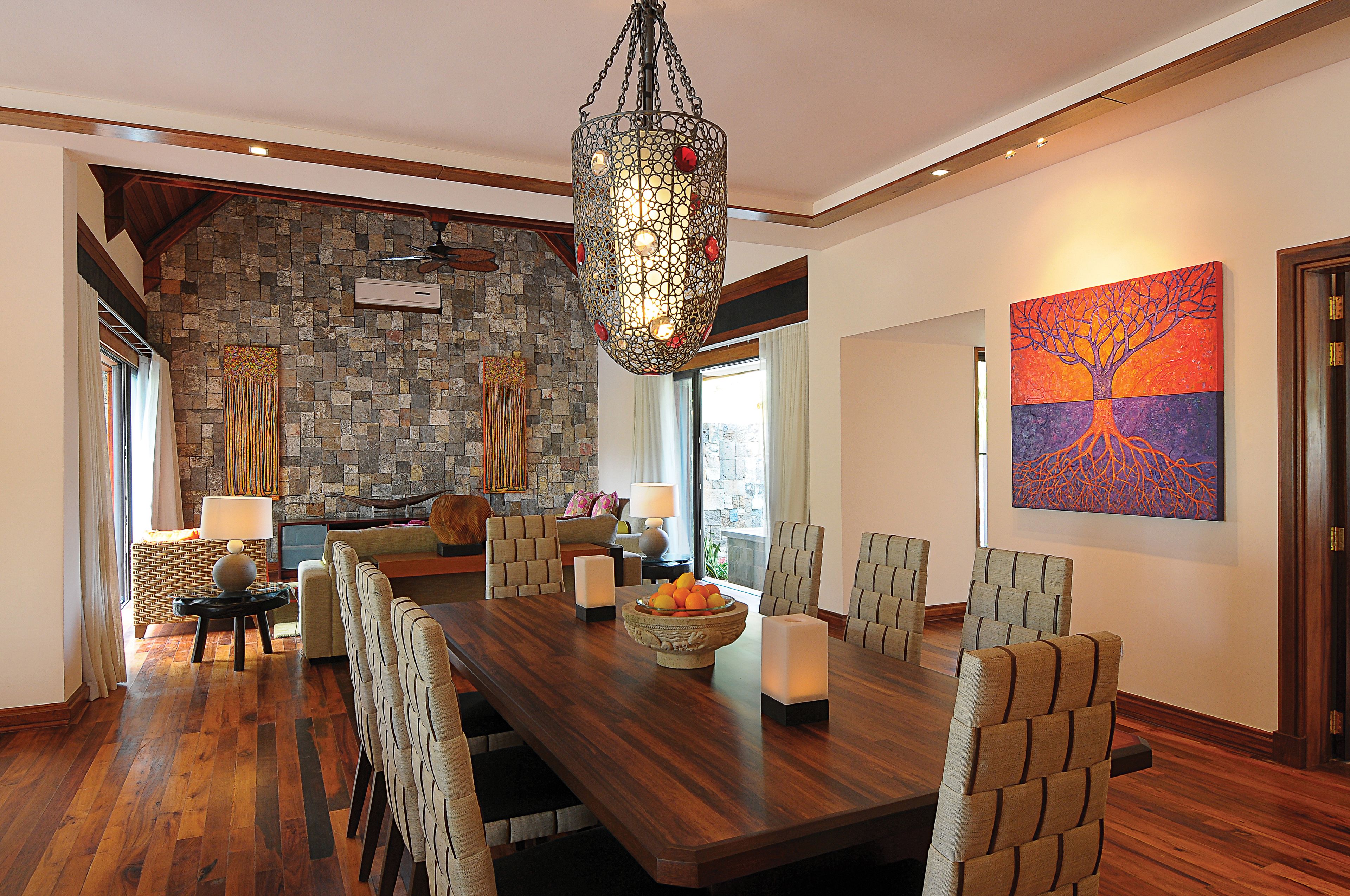 A spacious dining area with a large wooden table, comfortable chairs, a decorative hanging light fixture, and a stone wall.