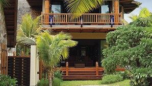 A traditional wooden house with a balcony, surrounded by lush greenery and a clear sky. - Sankhara Beachfront Villas (Poste Lafayette)