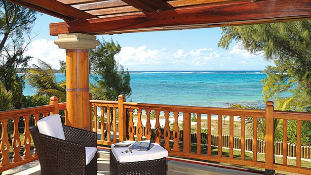 A wooden deck with wicker chairs and a table, overlooking a beach and ocean. - Sankhara Beachfront Villas (Poste Lafayette)