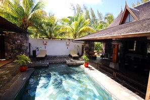 Un área de piscina con sillones de descanso, una pared de piedra y plantas tropicales.