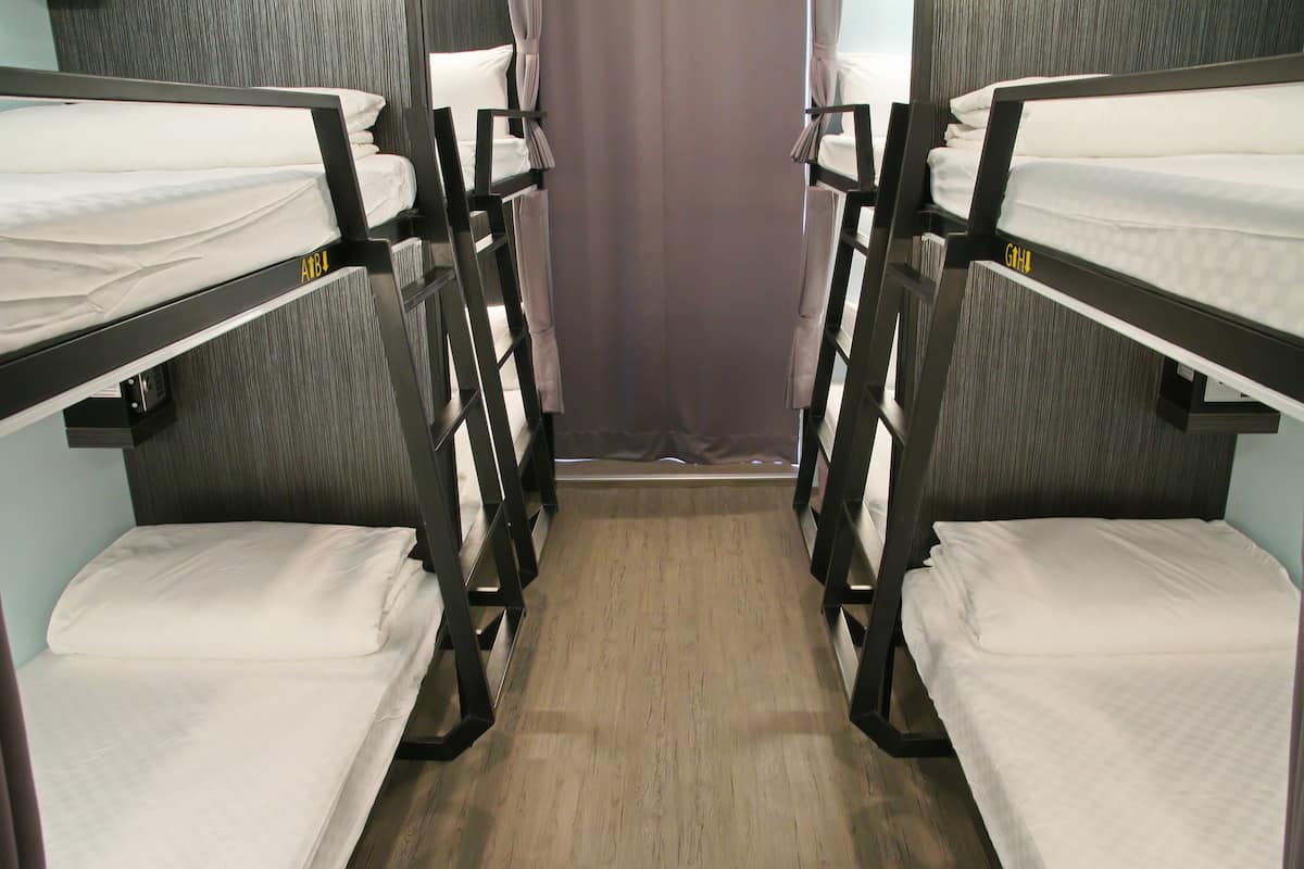 A room with bunk beds, each bed having a pillow and a blanket.